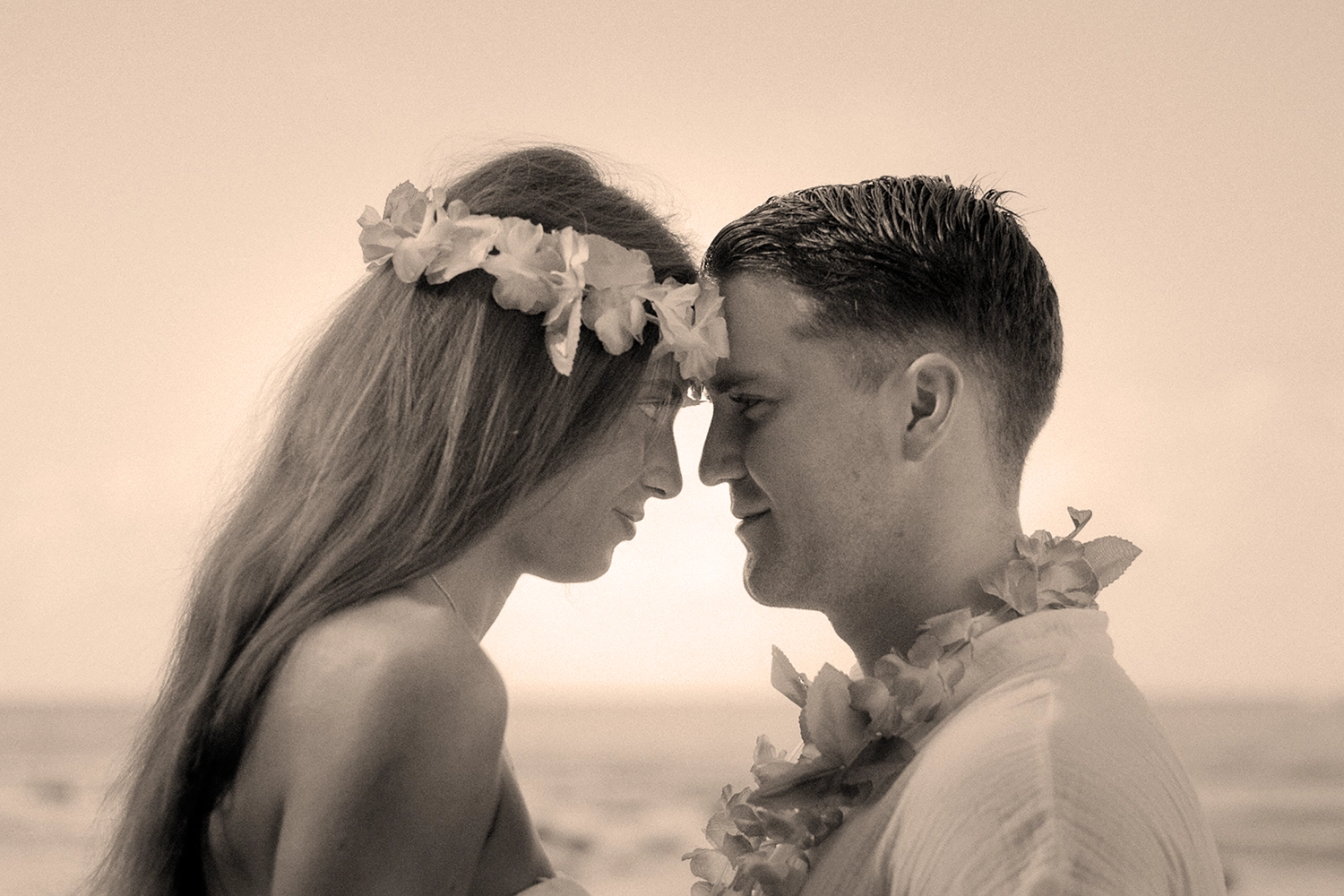 Retrato cercano y detallado de una pareja abrazada sonriendo frente al mar en una playa tropical.