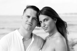 Primer plano artístico en blanco y negro de una pareja joven uniendo sus cabezas con el mar desenfocado al fondo en Playa del Carmen.