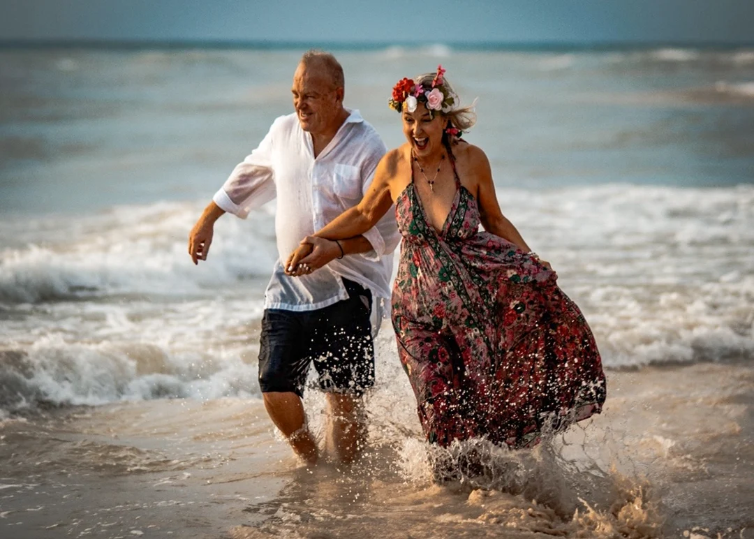 Couple running and laughing in the ocean during a romantic sunset beach photoshoot.