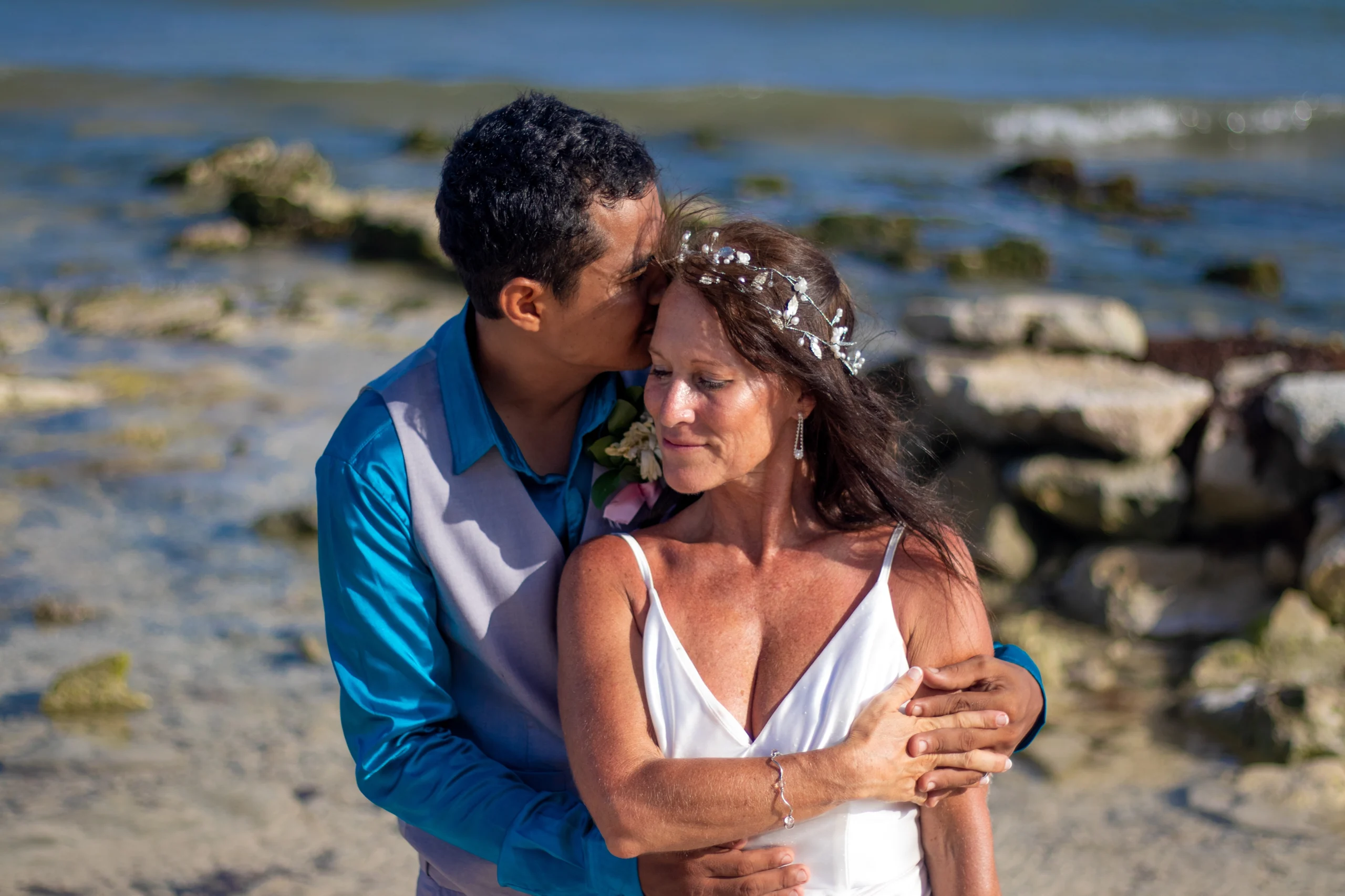 Pareja de novios corriendo emocionados hacia el mar en una playa tropical durante su sesión de bodas.