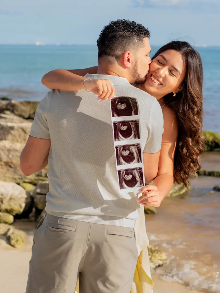 Primer plano de pareja abrazada en la playa durante sesión de maternidad