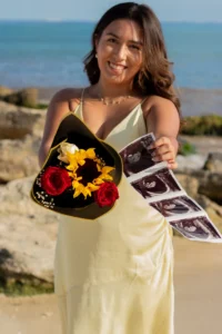Pregnant woman in yellow dress standing on rocky beach at sunset during maternity photo session in Playa del Carmen