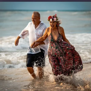 Couple running and laughing in the ocean during a romantic sunset beach photoshoot.